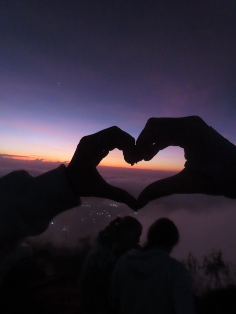 Holding up heart hands in front of the sunset at the top of Mount Batur Bali